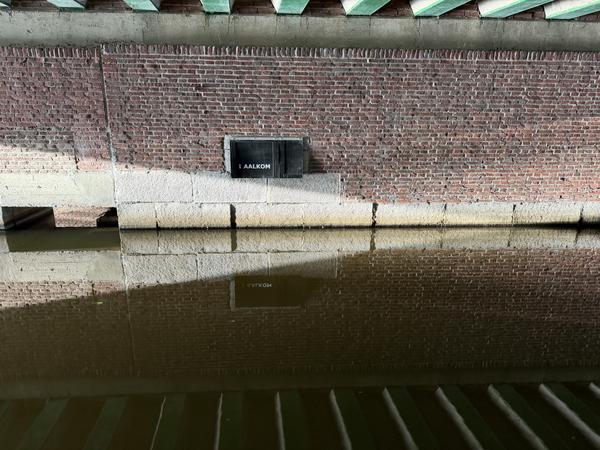 This photo captures a brick canal wall with a stone base, reflecting clearly in the calm water below at Weesperstraat, Weesperbuurt, Amsterdam